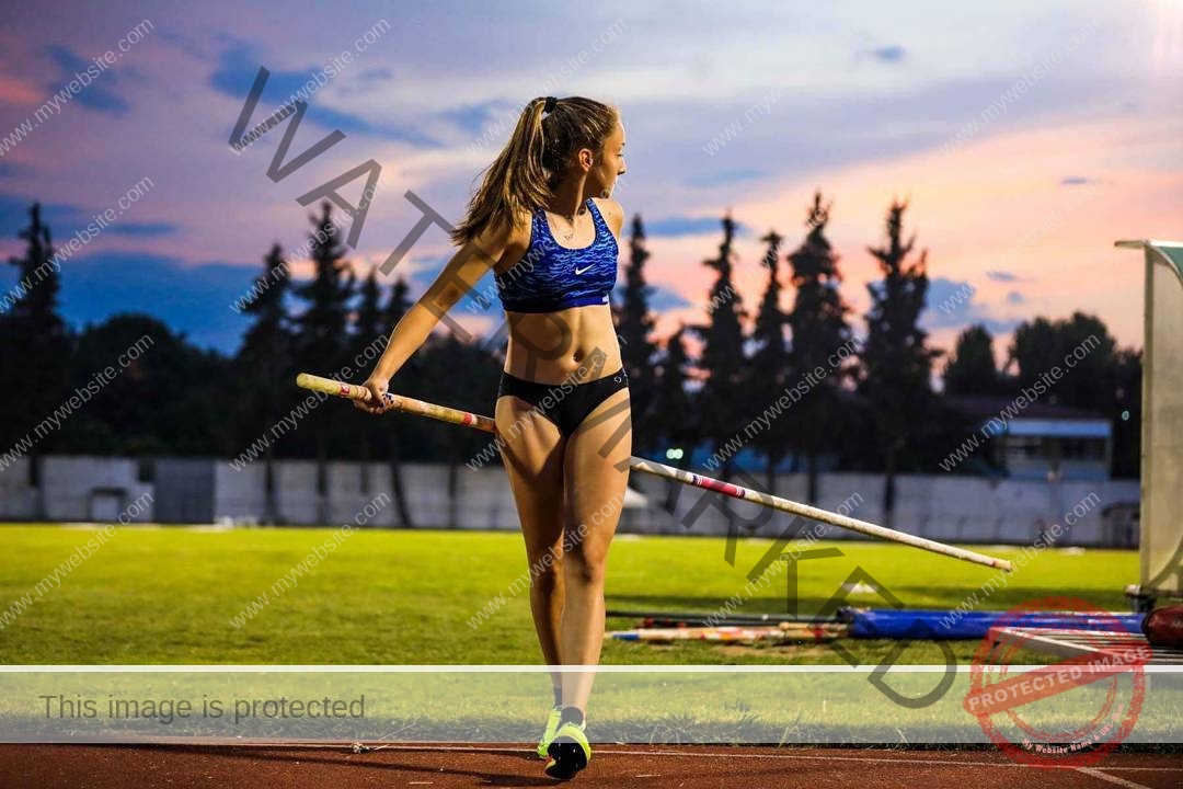ariadni-adamopoulou-greece-ariadni_adam-08995 Ariadni Adamopoulou, pole vaulter from Greece and Oklahoma State stands on a track holding a pole vault pole as the sun sets.