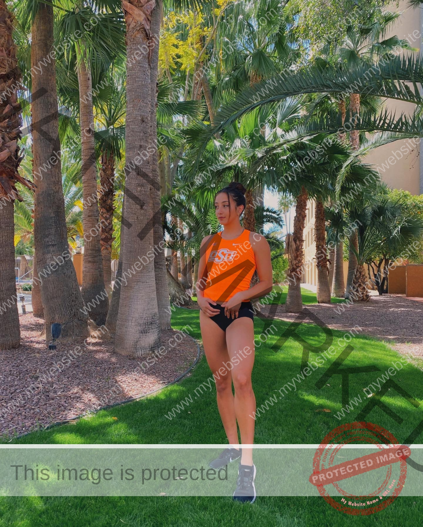 ariadni-adamopoulou-greece-ariadni_adam-09026 Ariadni Adamopoulou, pole vaulter from Greece and Oklahoma State, in an orange OSU tank top on grass among sunlit palm trees.