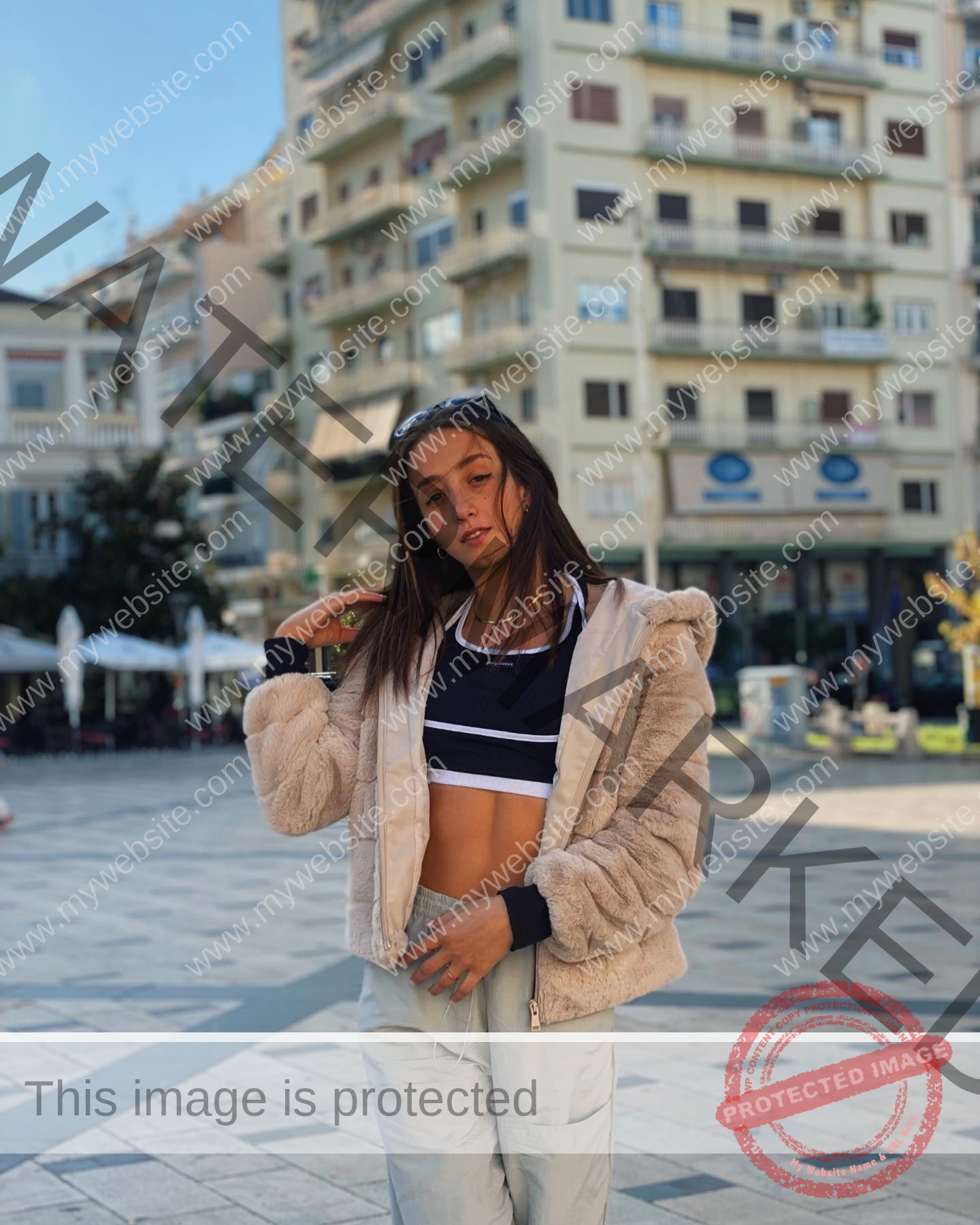 ariadni-adamopoulou-greece-ariadni_adam-09039 Ariadni Adamopoulou, pole vaulter from Greece, poses confidently in a light fur jacket and crop top in a sunny city square.