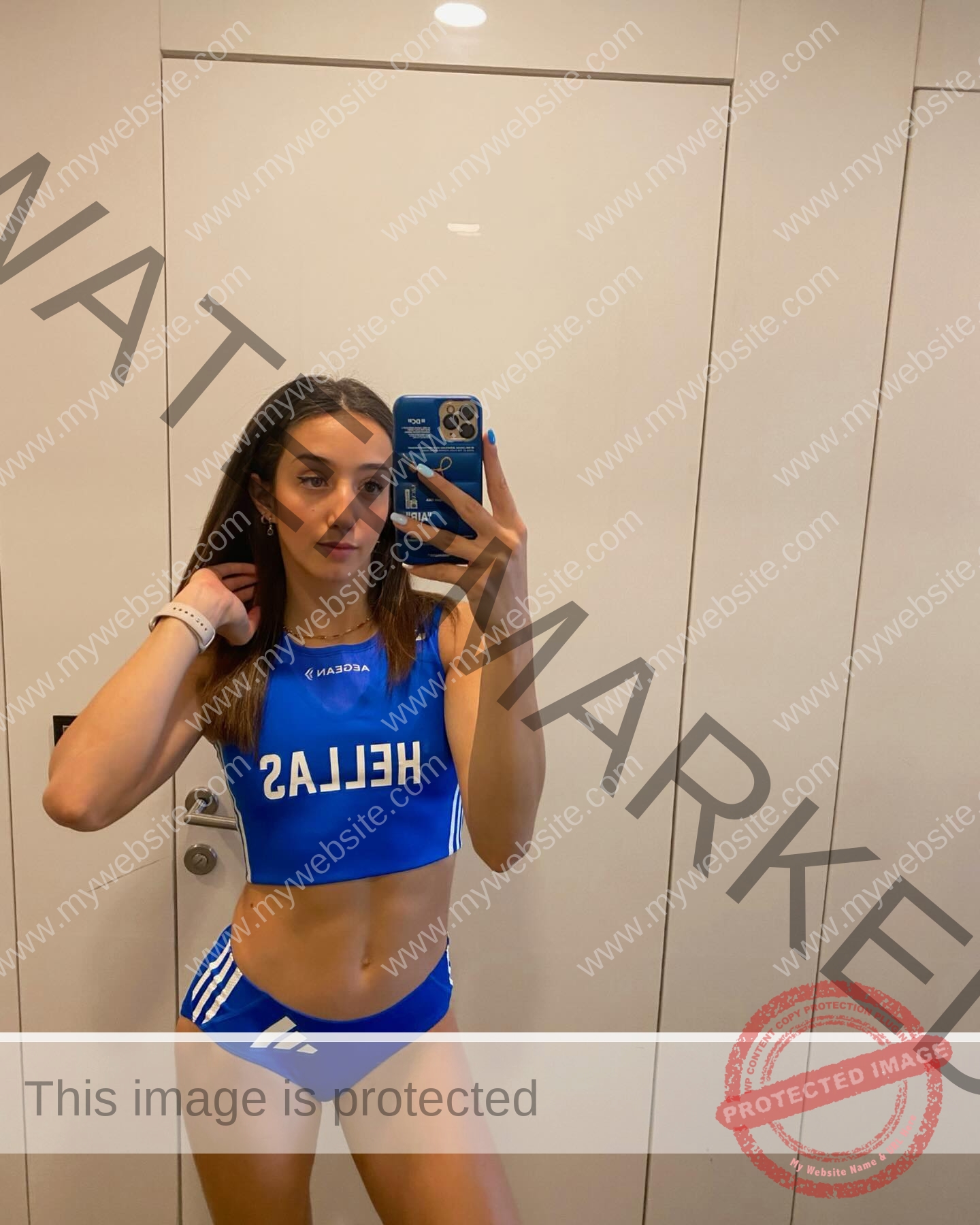 ariadni-adamopoulou-greece-ariadni_adam-09051 Ariadni Adamopoulou, pole vaulter from Greece and Oklahoma State, wears a blue HELLAS crop top and bikini, taking a mirror selfie.