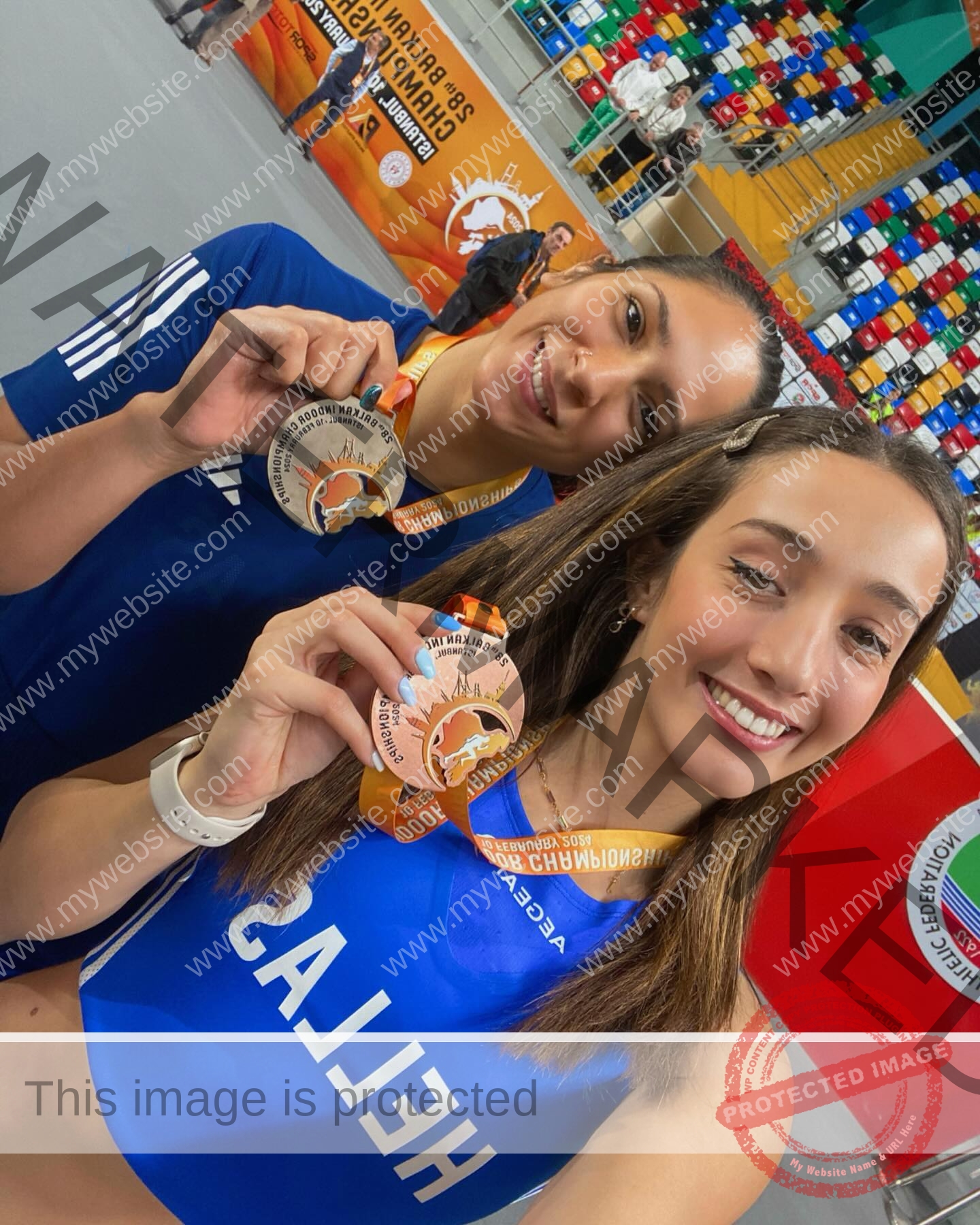 ariadni-adamopoulou-greece-ariadni_adam-09052 Ariadni Adamopoulou, pole vaulter from Greece, smiles in blue uniform with medals at an indoor event; "HELLAS" on one jersey.