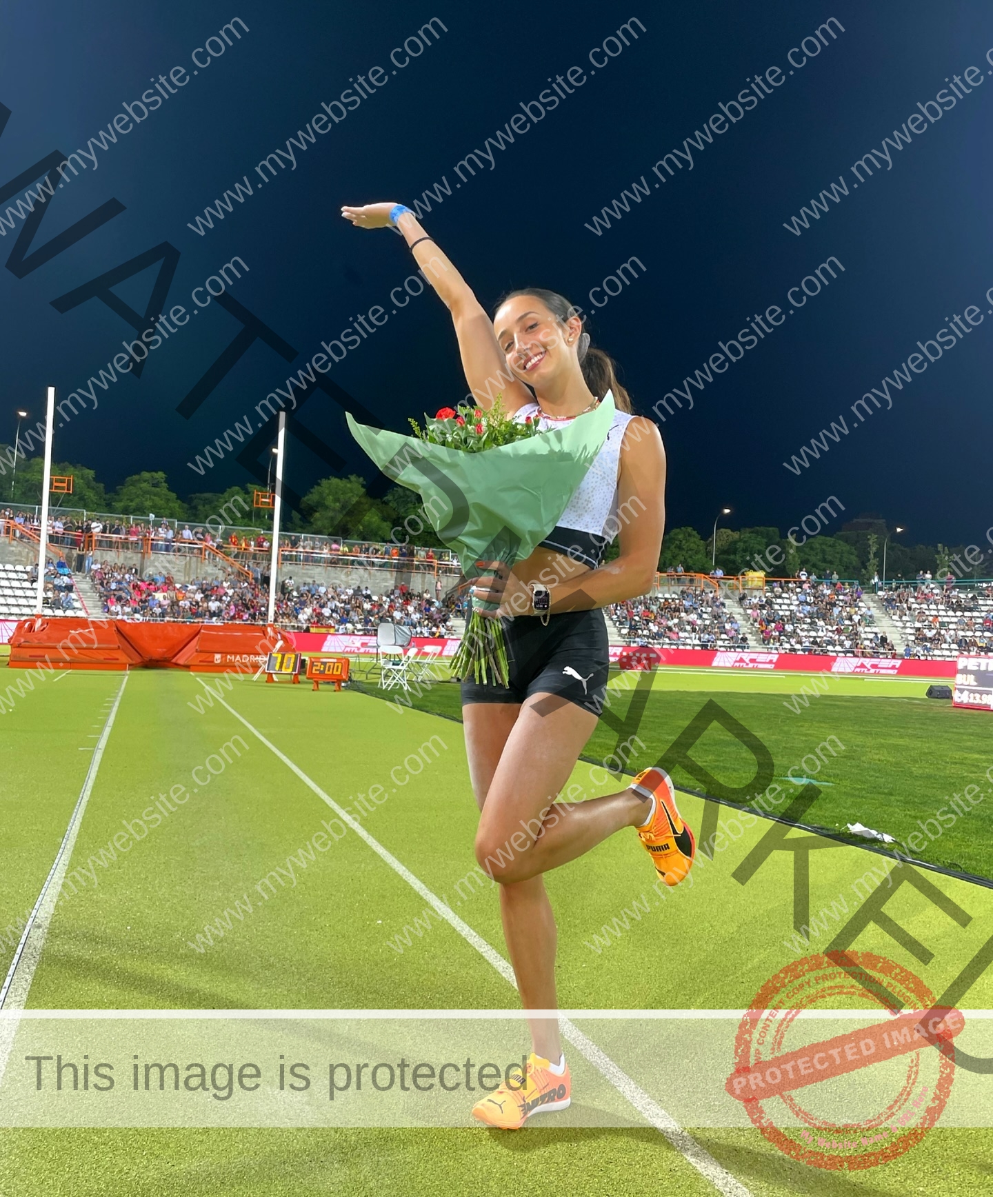ariadni-adamopoulou-greece-ariadni_adam-09080 Ariadni Adamopoulou, pole vaulter from Greece and Oklahoma State, poses playfully with flowers on a track; crowd in background.