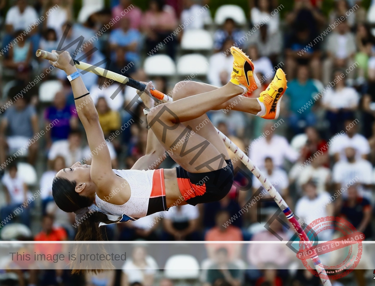ariadni-adamopoulou-greece-ariadni_adam-09088 Ariadni Adamopoulou, pole vaulter from Greece and Oklahoma State in mid-air vaults with bright orange shoes as spectators watch.