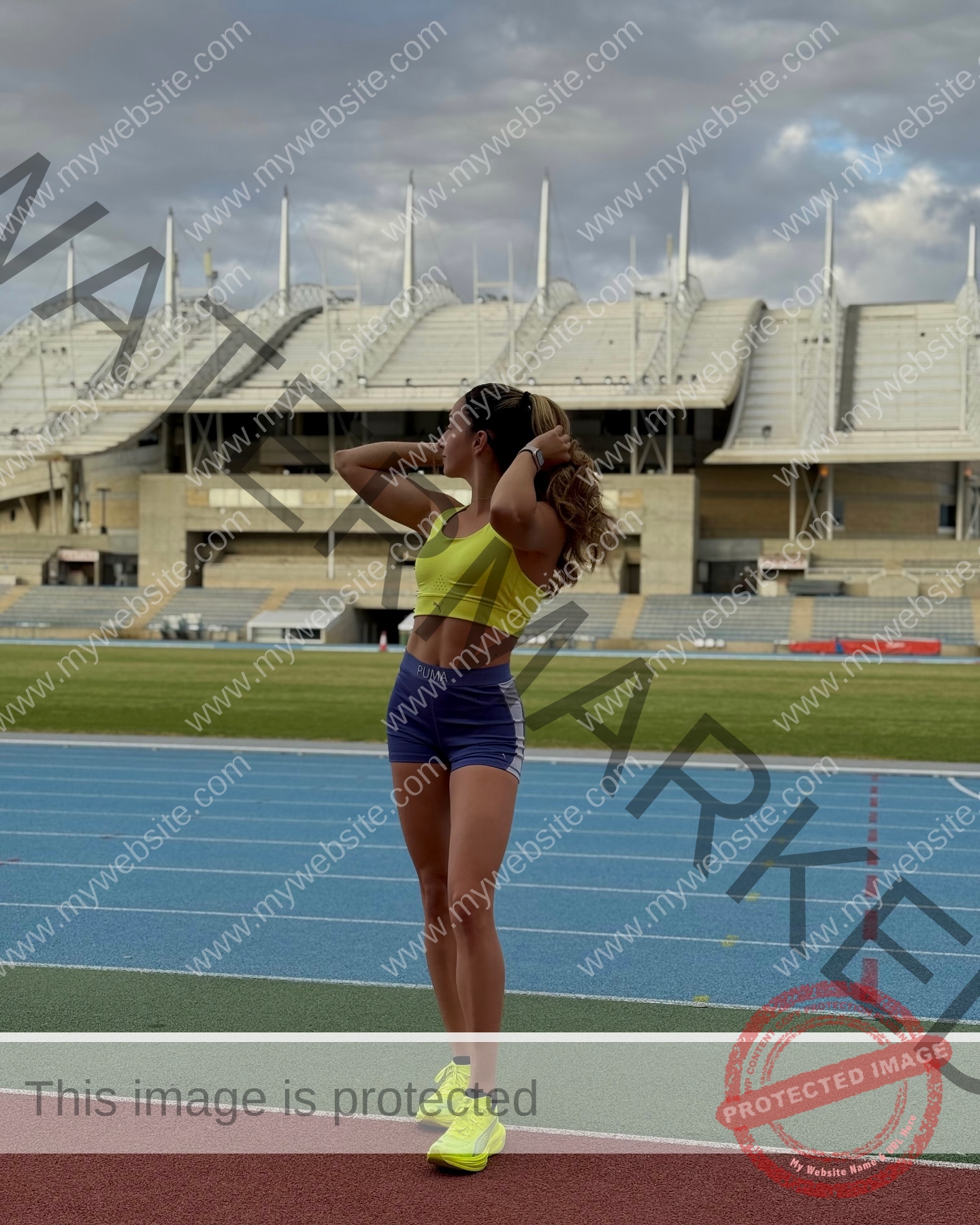 ariadni-adamopoulou-greece-ariadni_adam-09141 Ariadni Adamopoulou, pole vaulter from Greece and Oklahoma State, stands on a track in yellow sports bra and purple shorts.