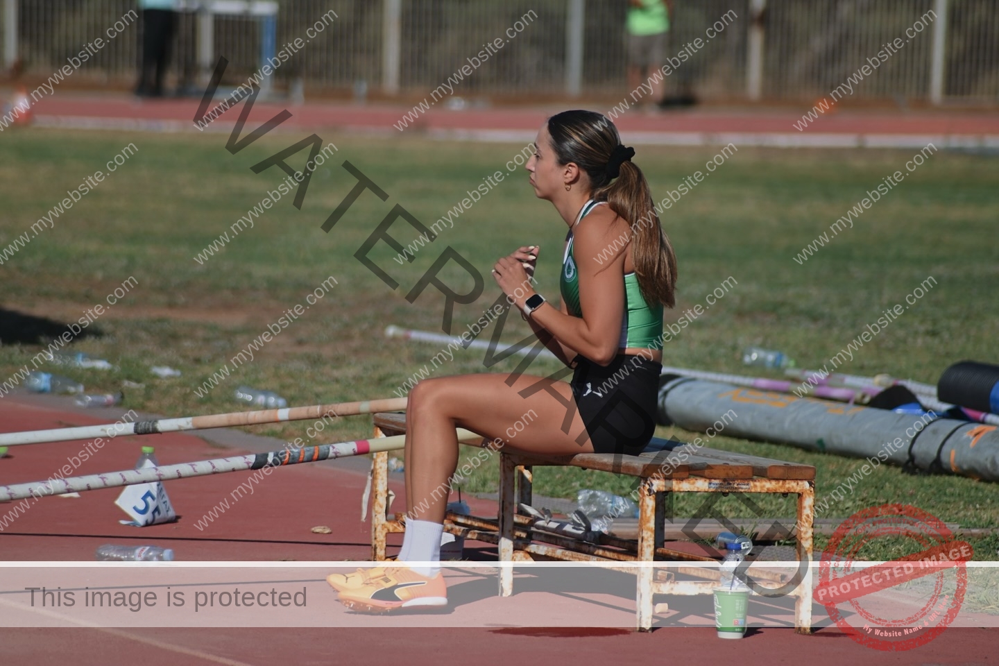 ariadni-adamopoulou-greece-ariadni_adam-09144 Ariadni Adamopoulou, pole vaulter from Greece and Oklahoma State, sits focused on a bench by the track with poles and gear nearby.