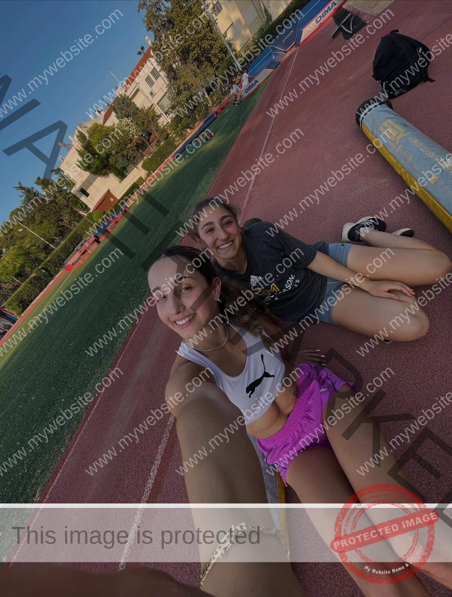ariadni-adamopoulou-greece-ariadni_adam-09155 Ariadni Adamopoulou, pole vaulter from Greece and Oklahoma State, sits smiling with another woman on an outdoor running track.