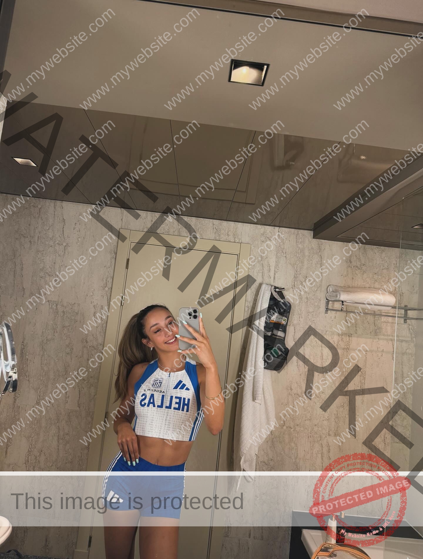 ariadni-adamopoulou-greece-ariadni_adam-09156 Ariadni Adamopoulou, pole vaulter from Greece and Oklahoma State, in a HELLAS athletic outfit taking a mirror selfie in a beige bathroom.