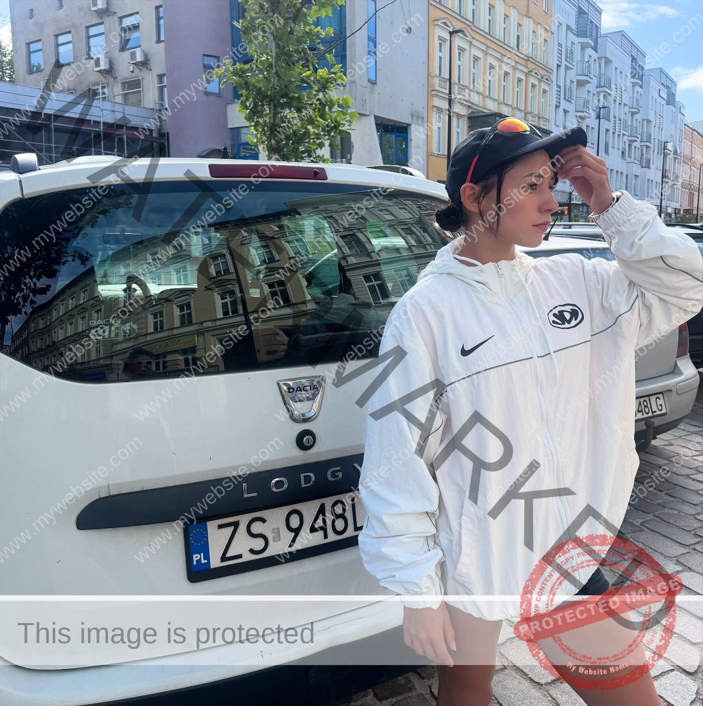 arie-aoki-japan-aokiarie_-x-09181 Arie Aoki, track star from Japan, wears a white Nike jacket and black shorts by a white Dacia Lodgy on a cobblestone city street.