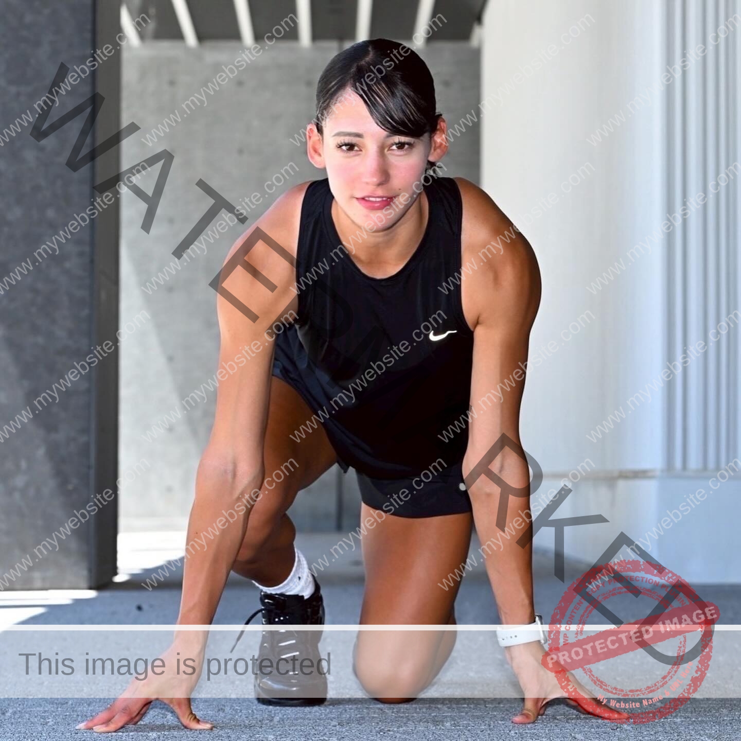 arie-aoki-japan-aokiarie_-x-09183 Arie Aoki, track star from Japan, crouches in a sprinter's starting pose on concrete, focused ahead; modern building behind.