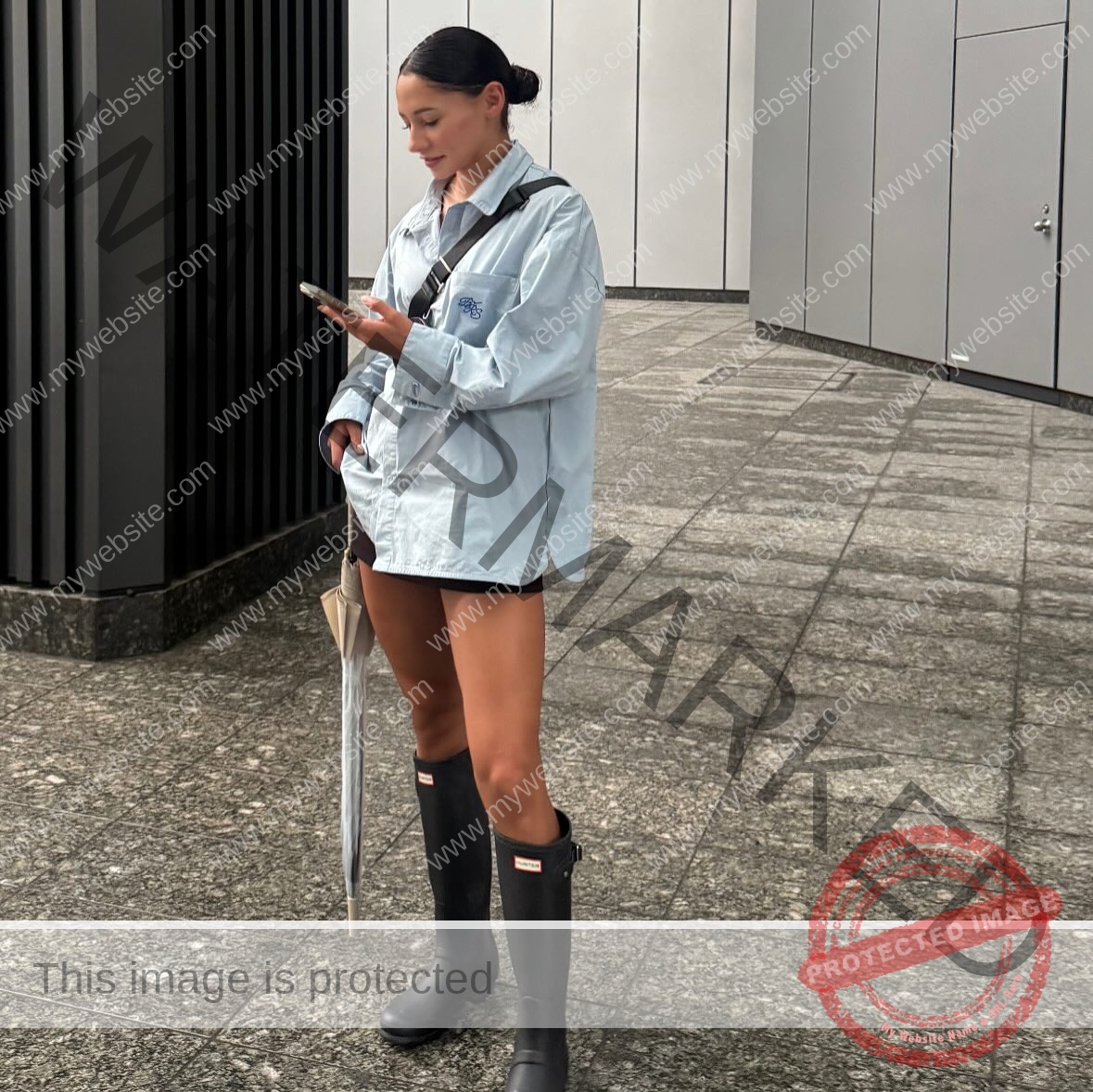 arie-aoki-japan-aokiarie_-x-09188 Arie Aoki, track star from Japan, stands on a city sidewalk in a blue oversized shirt, shorts, boots, and carries an umbrella.