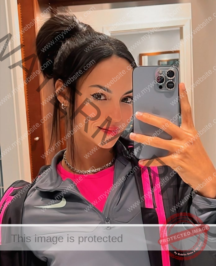 Basssant Hemida, track star from Egypt, takes a mirror selfie in a grey sports jacket with pink accents, smiling slightly.