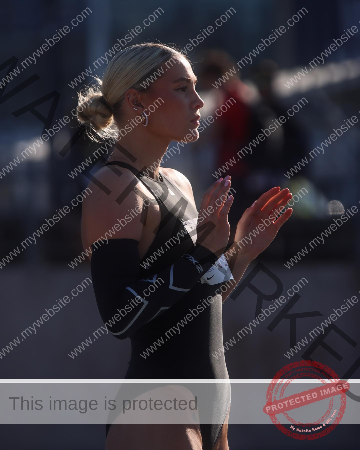 birna-kristjansdottir-iceland-birnakristink-10932 Birna-Kristjansdottir, track athlete from Iceland stands in black athletic suit outdoors, clapping, sunlight on her low-bun profile.