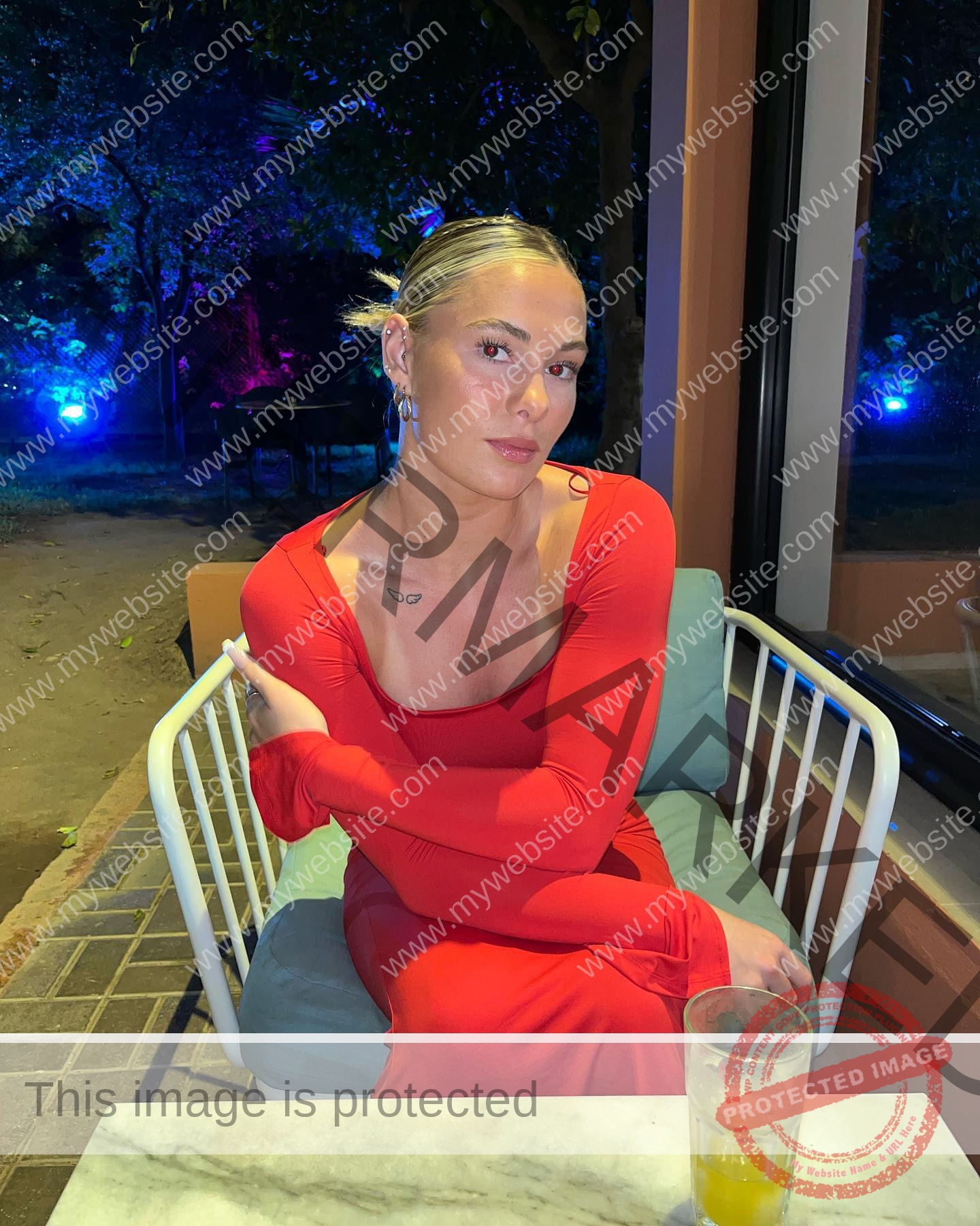 birna-kristjansdottir-iceland-birnakristink-10944 Birna-Kristjansdottir, track athlete from Iceland, sits in a red dress at an outdoor table with juice, colorful lights behind her at night.