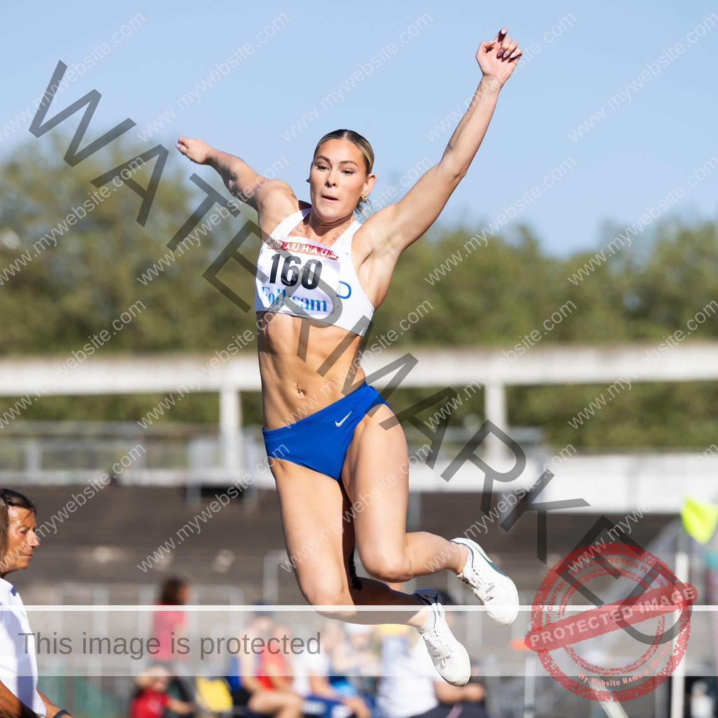birna-kristjansdottir-iceland-birnakristink-10963 Birna-Kristjansdottir, track athlete from Iceland, in blue shorts and white top, number 160, mid-air long jumping at a stadium.