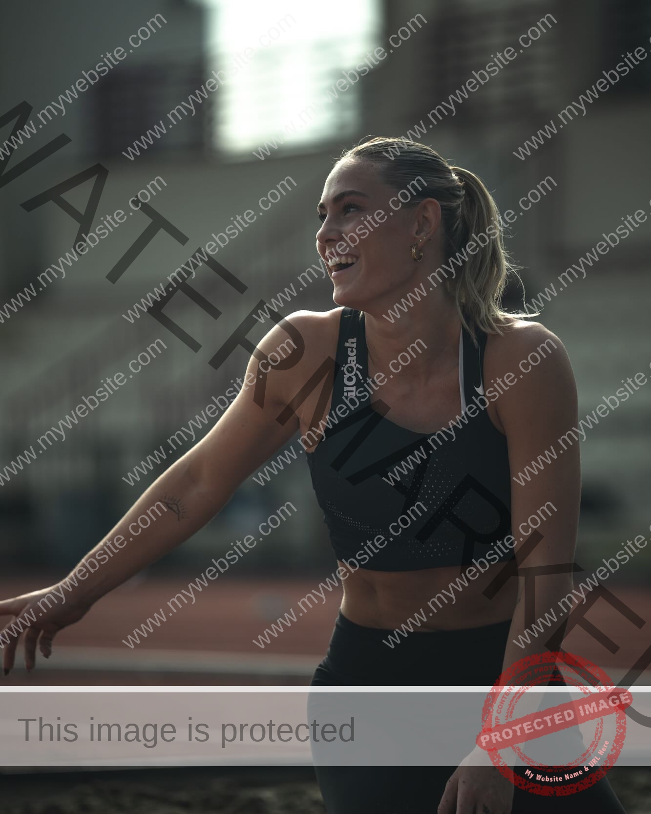 birna-kristjansdottir-iceland-birnakristink-11020 Birna-Kristjansdottir, track athlete from Iceland, smiles in athletic wear on a running track with stadium seats blurred behind her.