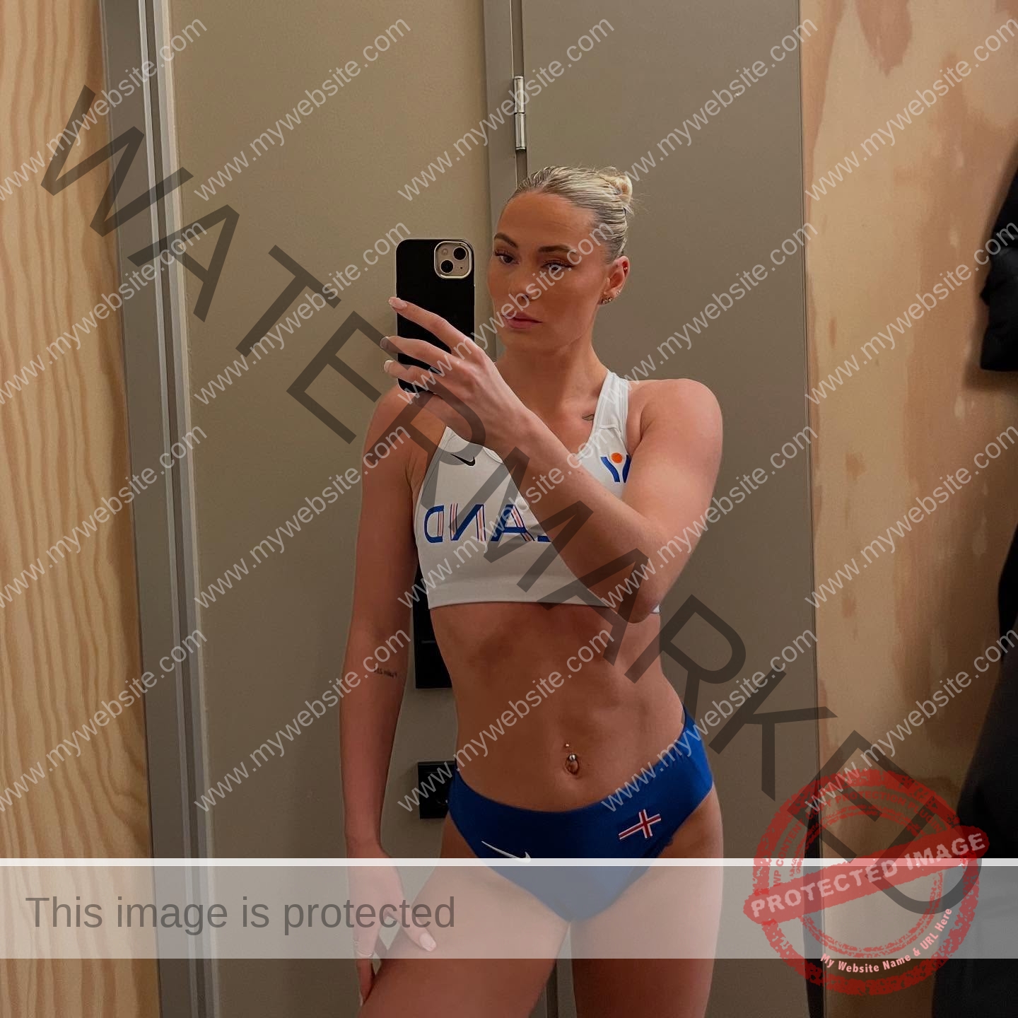 birna-kristjansdottir-iceland-birnakristink-11027 Birna-Kristjansdottir, track athlete from Iceland, wears a sports bikini with ICELAND and poses for a mirror selfie in a wood-paneled room.