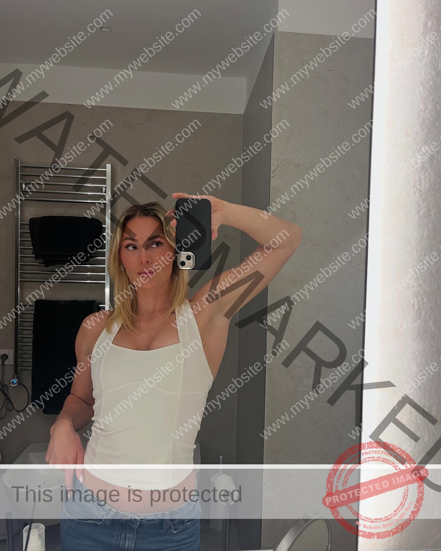 birna-kristjansdottir-iceland-birnakristink-11040 Birna-Kristjansdottir, track athlete from Iceland, with blonde hair takes a mirror selfie in a bathroom, wearing white top and blue jeans.