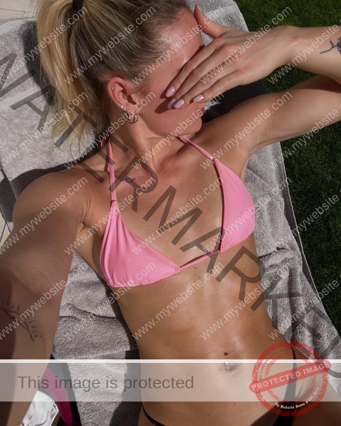 Birna-Kristjansdottir, track athlete from Iceland, sunbathes in pink bikini and black bottoms, tattoos and navel piercing visible.