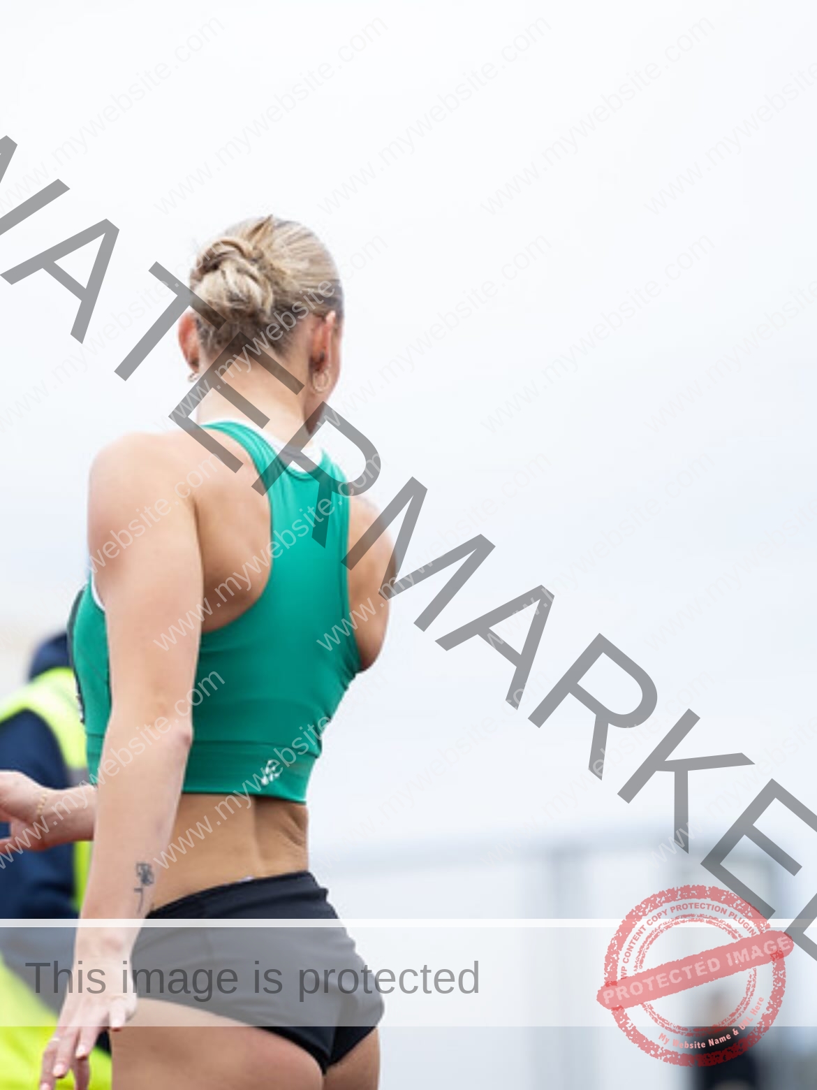 birna-kristjansdottir-iceland-birnakristink-11084 Birna-Kristjansdottir, track athlete from Iceland, stands outdoors in a green crop top and black shorts, hair in a bun, preparing.