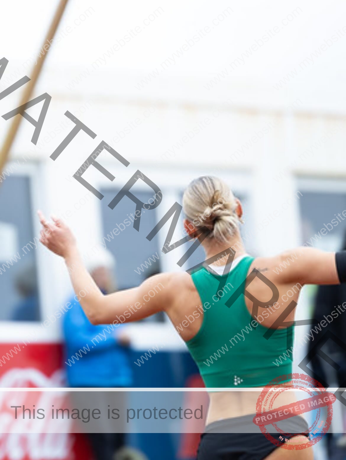 birna-kristjansdottir-iceland-birnakristink-11085 Birna-Kristjansdottir, track athlete from Iceland, stands outdoors with arms raised, seen from behind in green top and black shorts.