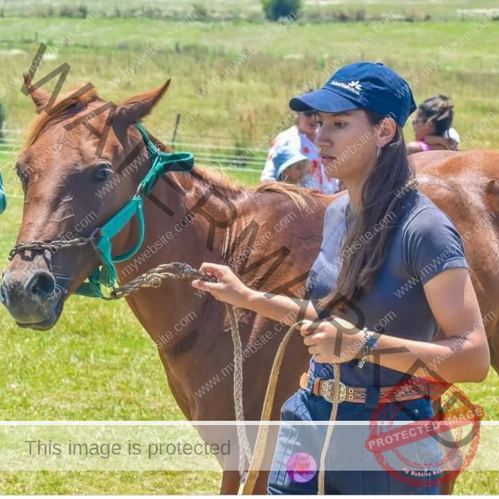brandy-romero-uruguay-brandy_rom08-0040 Brandy Romero Brandy Romero, in a navy cap and casual clothes, leads a brown horse with a rope across a grassy field in Uruguay.