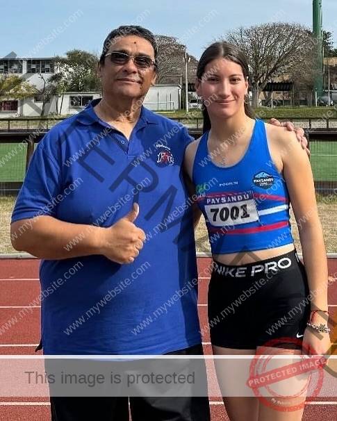 brandy-romero-uruguay-brandy_rom08-0080 Brandy Romero A man in a blue polo shirt stands next to Brandy Romero in a blue sports top and black shorts on an outdoor track, both smiling.