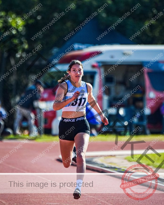 Brandy Romero Brandy Romero, a female track and field athlete from Uruguay, wearing bib 317 and a blue-white top, sprints on an outdoor track with an ambulance and people blurred in the background.