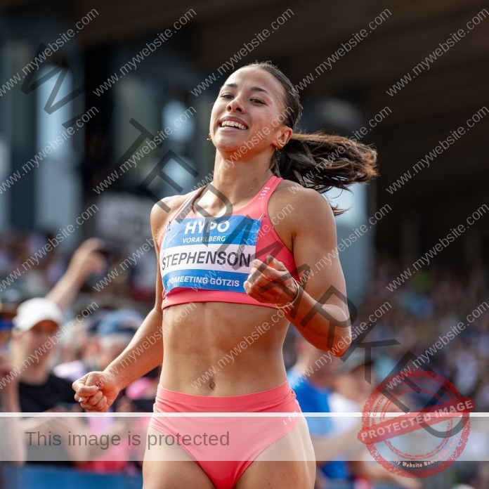 Briana Stephenson A female track and field athlete in pink smiles as she crosses the finish line in New Zealand, crowd cheering.