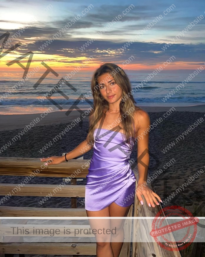 Cam Ruffini Cam Ruffini captures a woman in a shiny lavender dress on a beach railing at sunset, waves and colorful sky behind her.