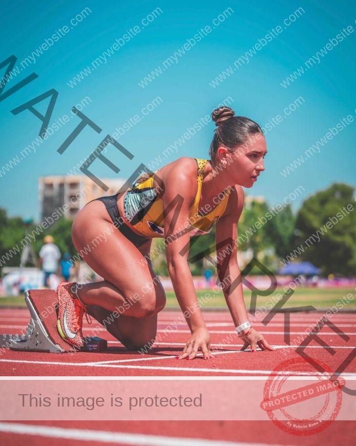 Camila Pagani A female track and field athlete in running gear is poised at the starting blocks on a Spanish track, ready to race.