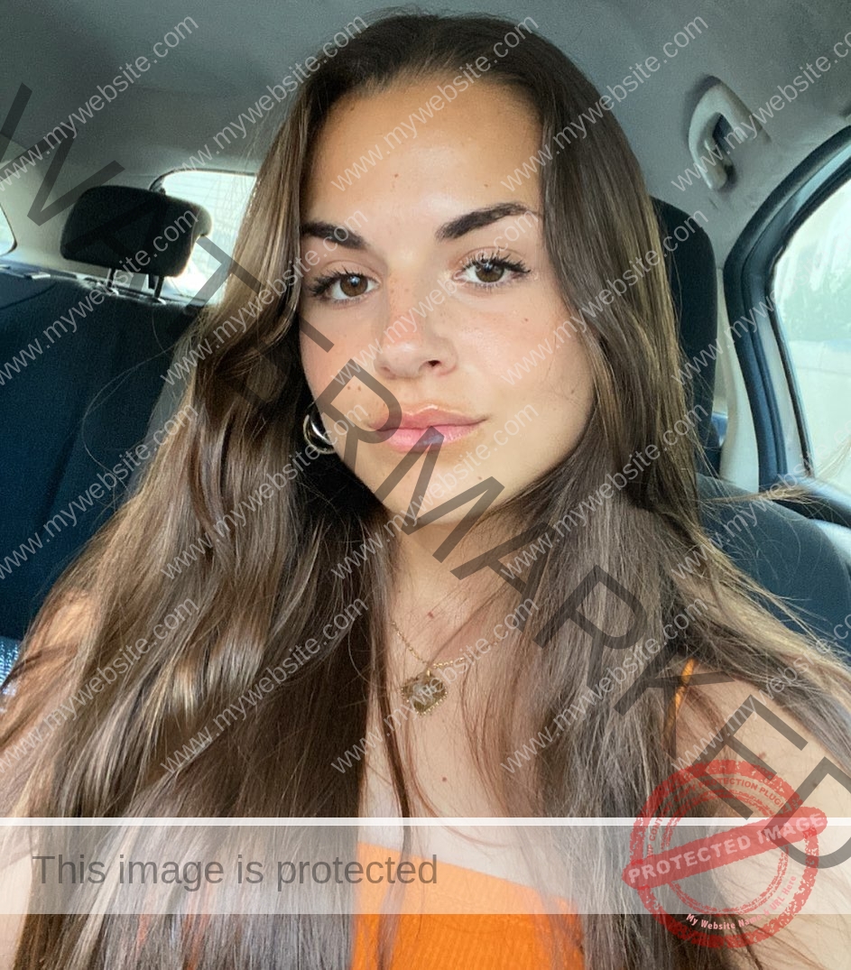 carla-scicluna-malta-carla.scicluna-01697 Carla Scicluna, track athlete from Malta, with long brown hair and a bright orange top sits in a car, looking relaxed at the camera.