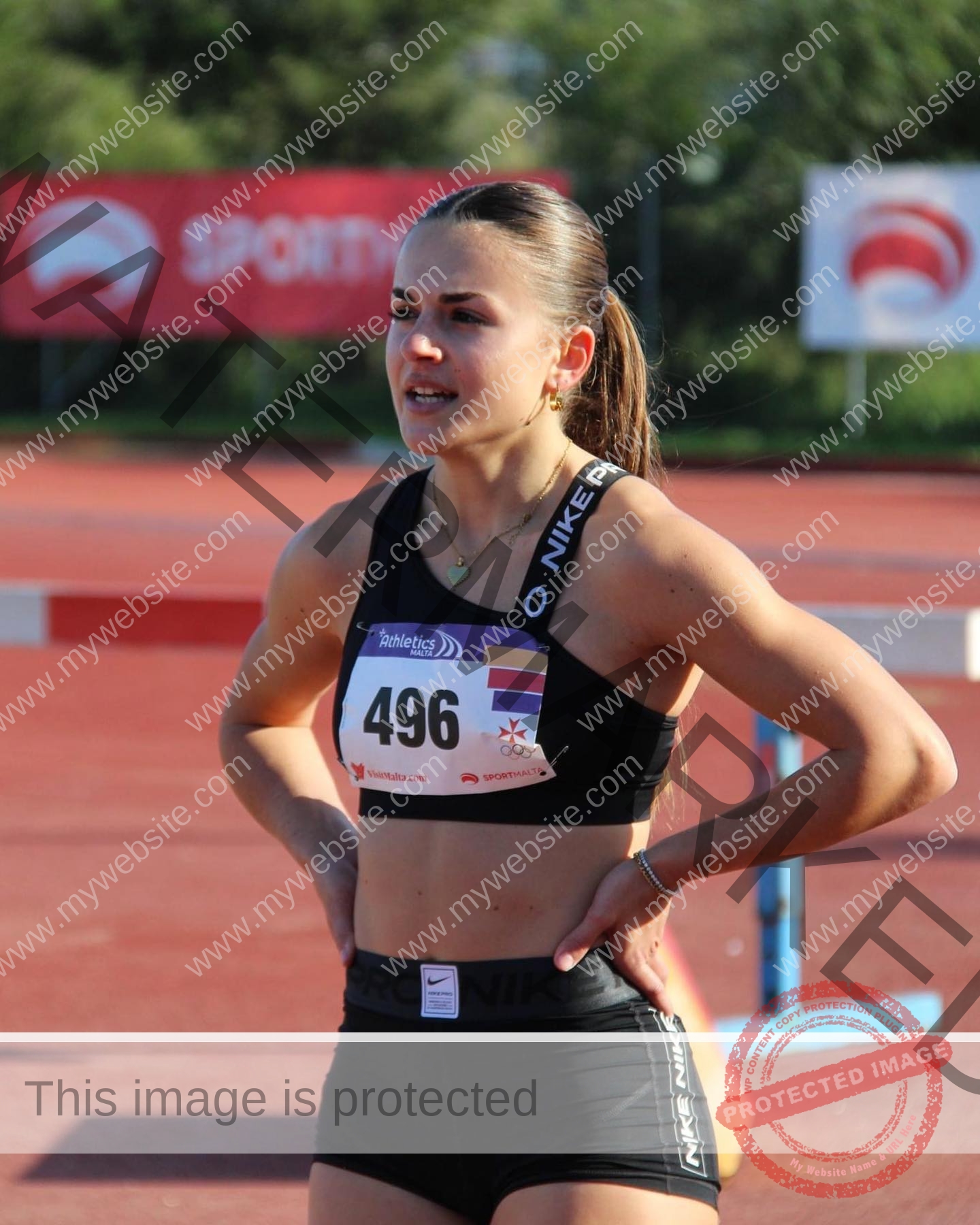 carla-scicluna-malta-carla.scicluna-01716 Carla Scicluna, track athlete from Malta, stands in a black sports outfit with bib 496 on a red track, hands on hips, looking focused.