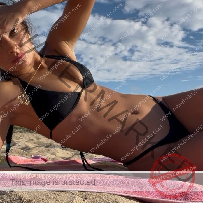 Channary Royal A person wearing a black bikini lies on an Australian beach, shielding their eyes from the sun, pink towel beneath them.