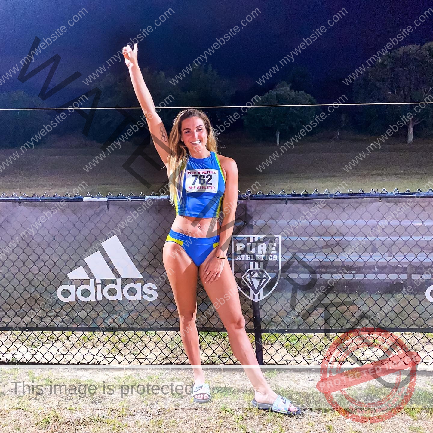 charlotte-wingfield-malta-charlottewingfield.oly-03724 Charlotte Wingfield, track athlete from Malta, in blue and yellow uniform, smiles and raises a finger near Adidas logos on a night field.