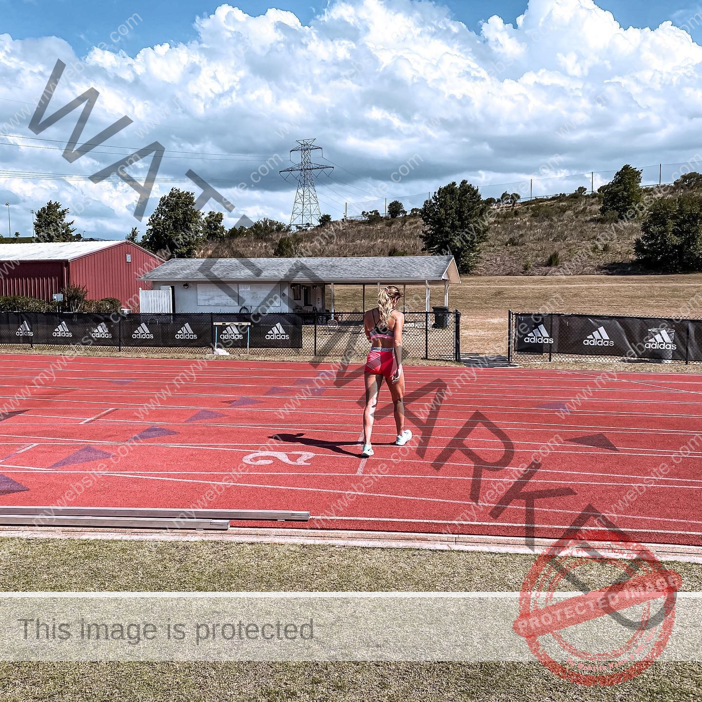 charlotte-wingfield-malta-charlottewingfield.oly-03728 Charlotte Wingfield, track athlete from Malta, stands alone on a running track in red sportswear, facing away under partly cloudy skies.