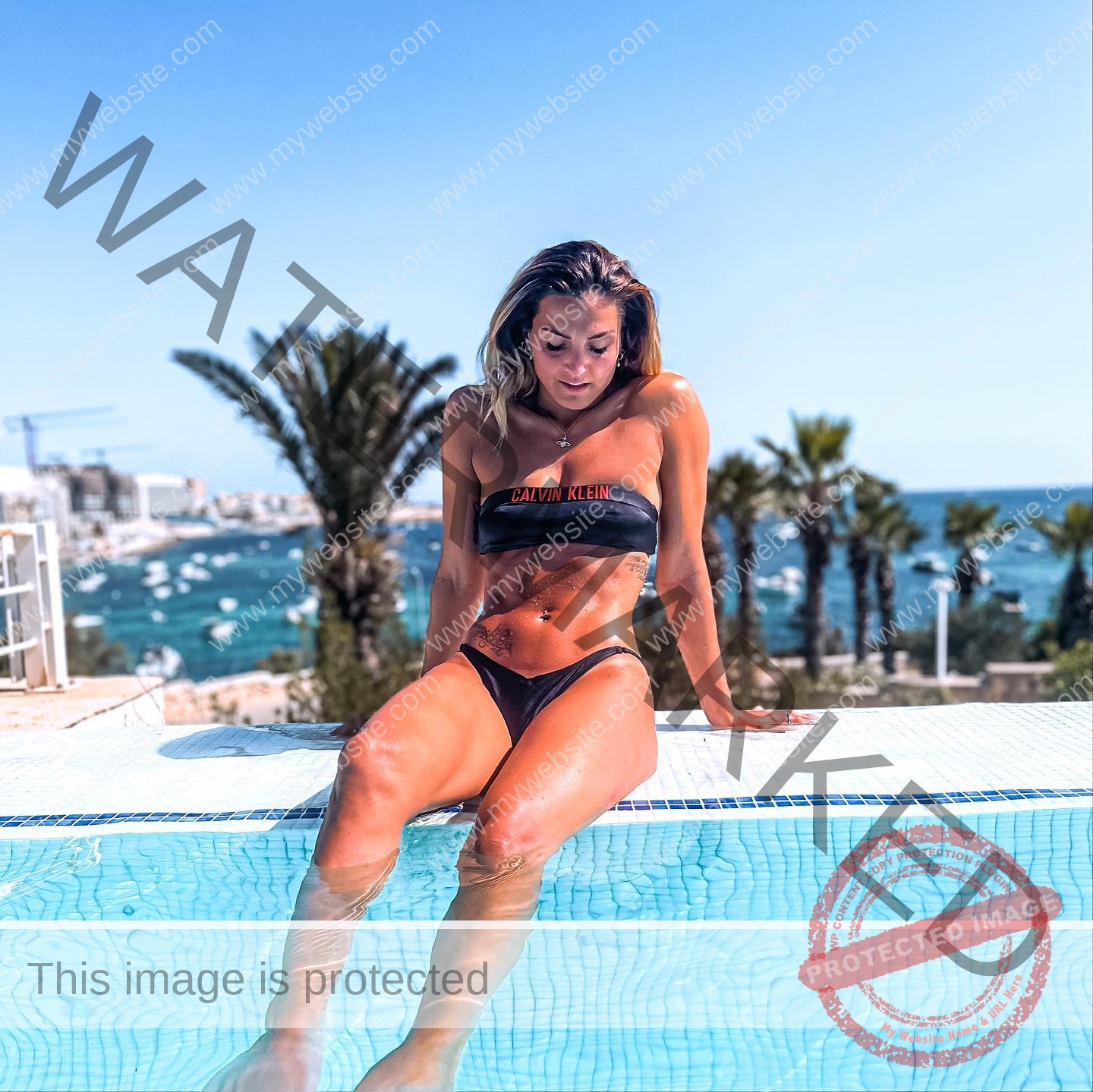 charlotte-wingfield-malta-charlottewingfield.oly-03735 Charlotte Wingfield, track athlete from Malta, sits poolside in a black bikini, legs in water, amid palms and boats on a sunny coast.