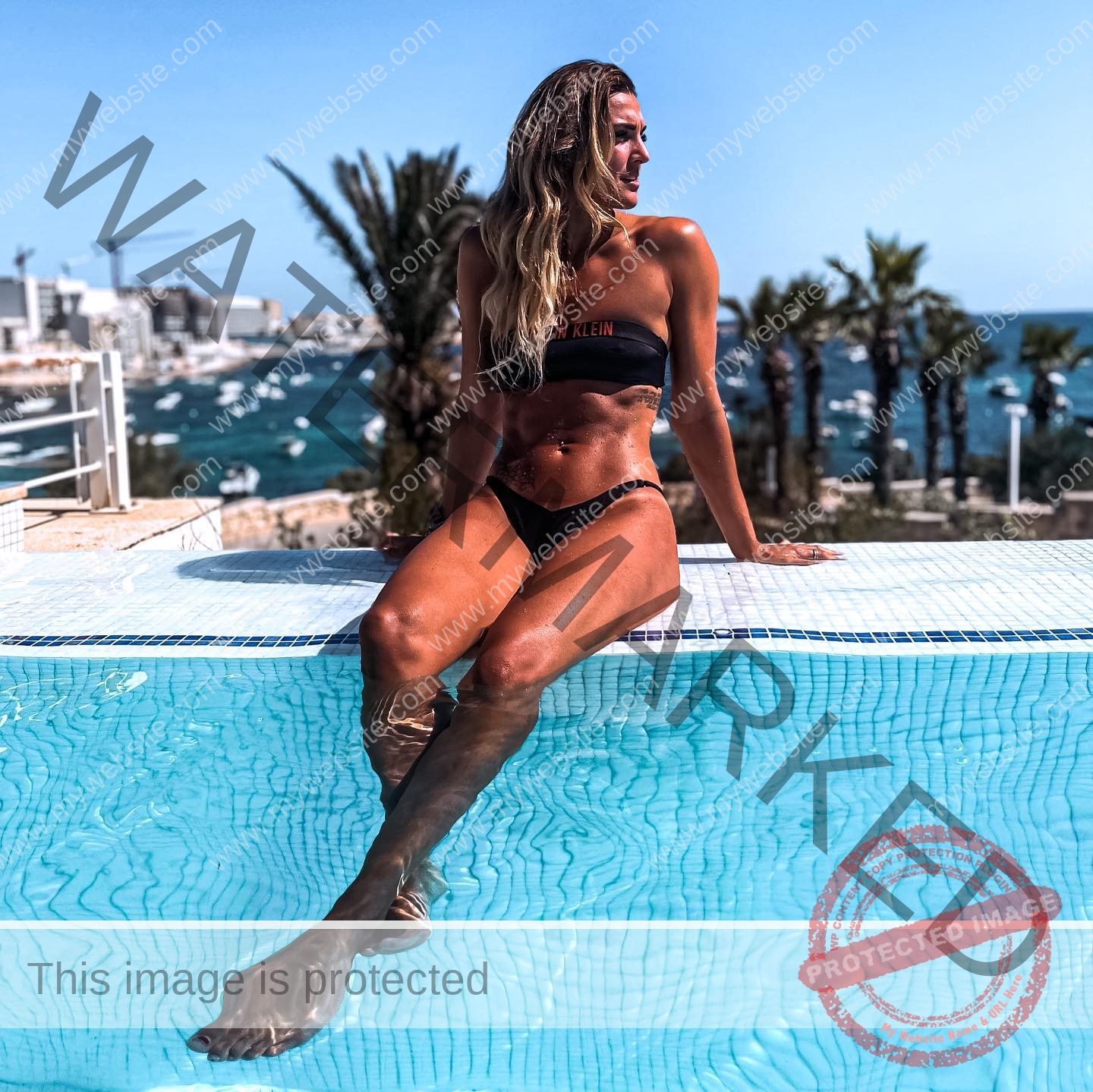 charlotte-wingfield-malta-charlottewingfield.oly-03736 Charlotte Wingfield, track athlete from Malta, sits in a black bikini poolside, one leg in the water, looking aside; palm trees and a marina behind.