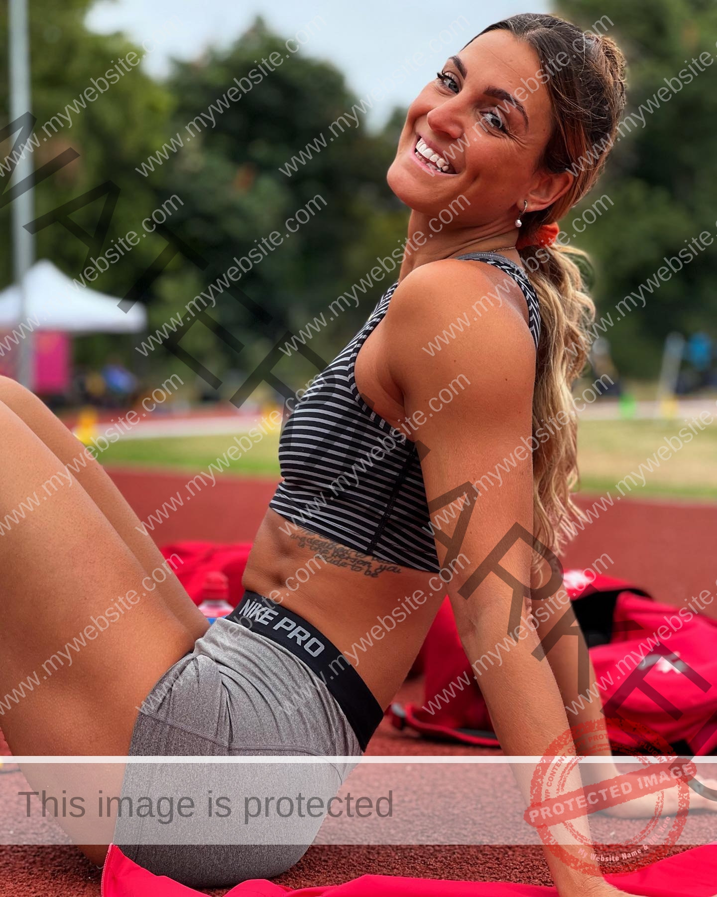 charlotte-wingfield-malta-charlottewingfield.oly-03757 Charlotte Wingfield, track athlete from Malta, sits on a running track in striped sports bra and gray Nike Pro shorts, smiling.