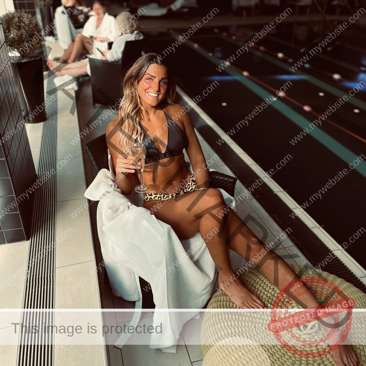 charlotte-wingfield-malta-charlottewingfield.oly-03779 Charlotte Wingfield, track athlete from Malta, sits on a lounge chair by an indoor pool in a bikini, smiling with a drink in hand.