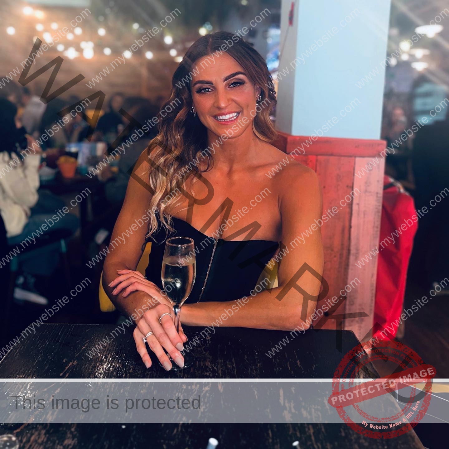 charlotte-wingfield-malta-charlottewingfield.oly-03795 Charlotte Wingfield, track athlete from Malta, with long wavy hair, sits at a dark table in a lively restaurant holding sparkling wine.