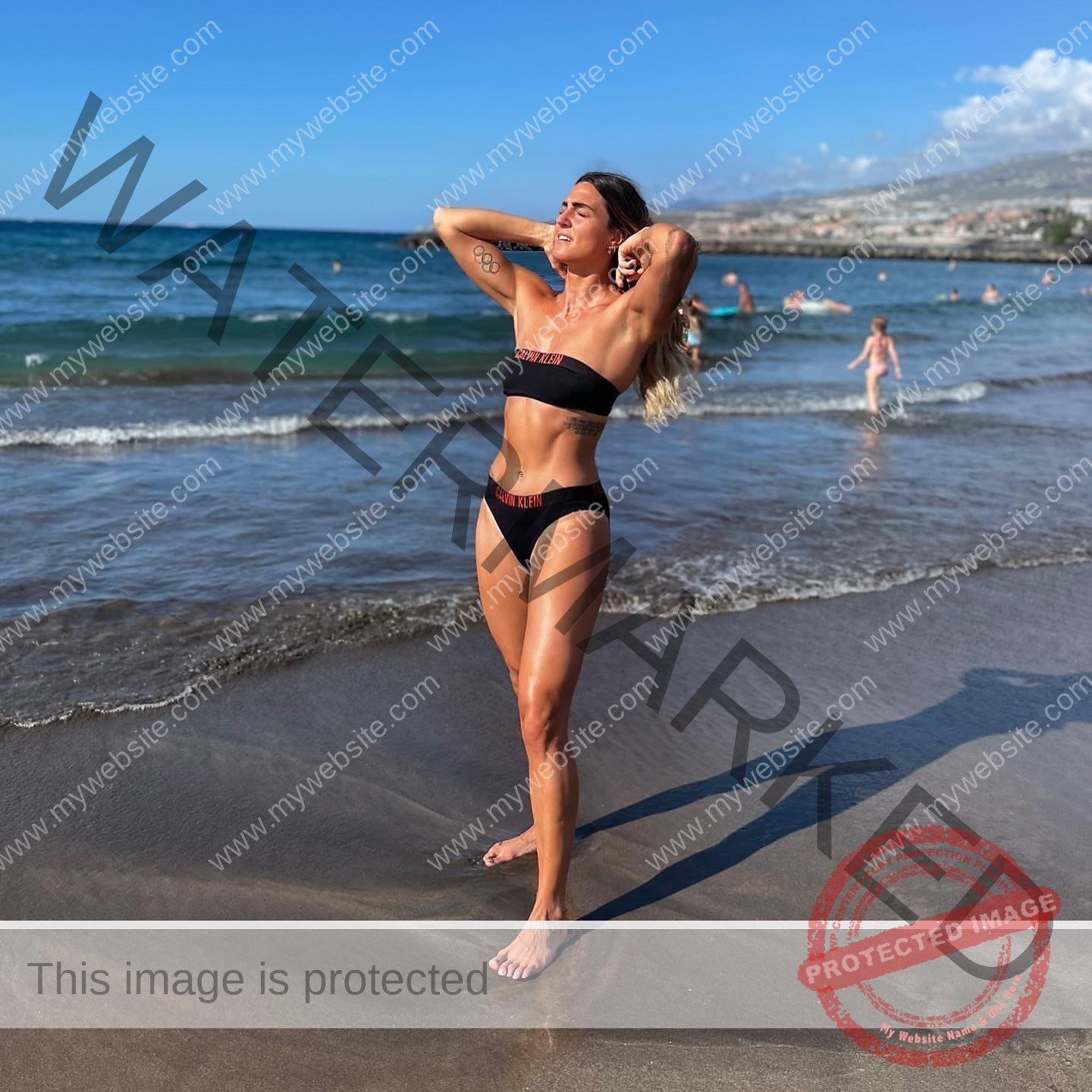 charlotte-wingfield-malta-charlottewingfield.oly-03810 Charlotte Wingfield, track athlete from Malta, in a black bikini stands on a sandy beach with eyes closed, ocean and sky behind.