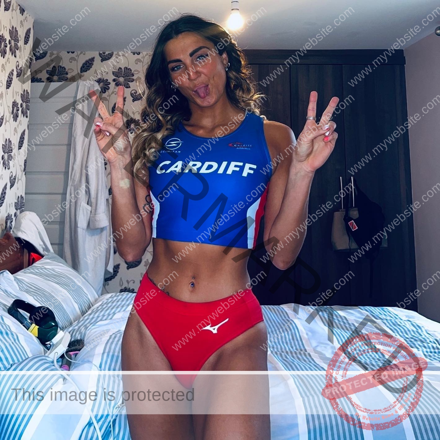 charlotte-wingfield-malta-charlottewingfield.oly-03814 Charlotte Wingfield, track athlete from Malta, wears a blue Cardiff crop top and red briefs, smiling with peace signs in a bedroom.