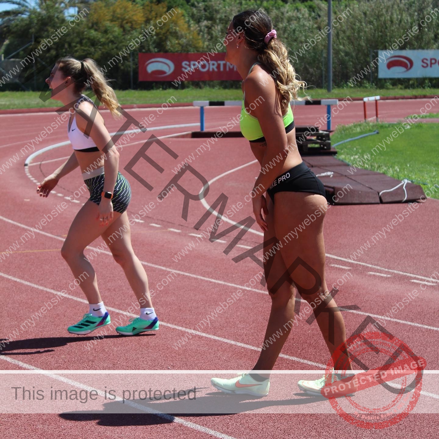 charlotte-wingfield-malta-charlottewingfield.oly-03833 Charlotte Wingfield, track athlete from Malta, stands on a red outdoor track with another woman, ready to race; greenery and SPORTMAX signs.