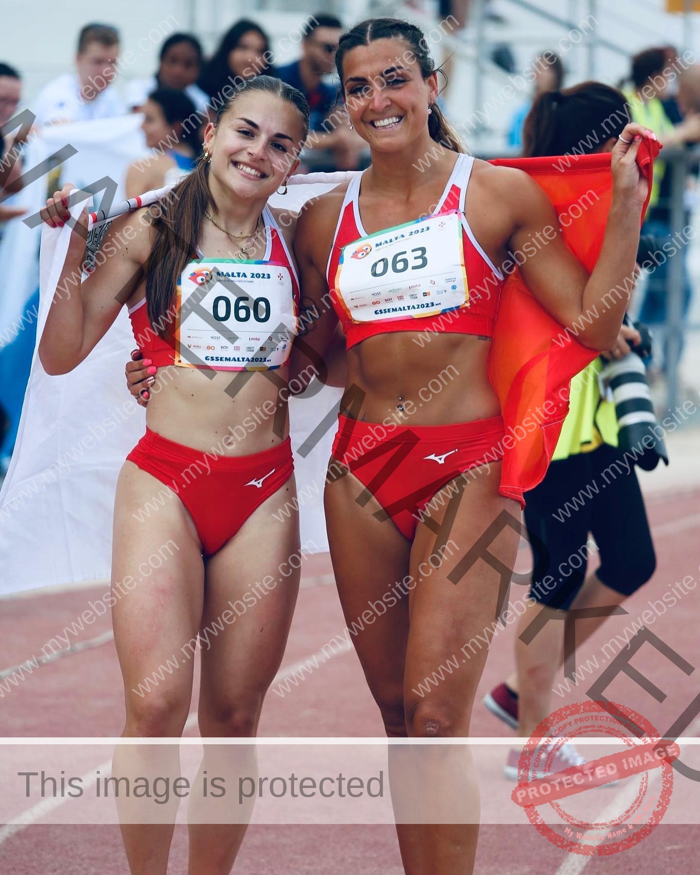 charlotte-wingfield-malta-charlottewingfield.oly-03866 Charlotte Wingfield, track athlete from Malta, with another woman in red sportswear holding flags on a running track, bibs 060 & 063.