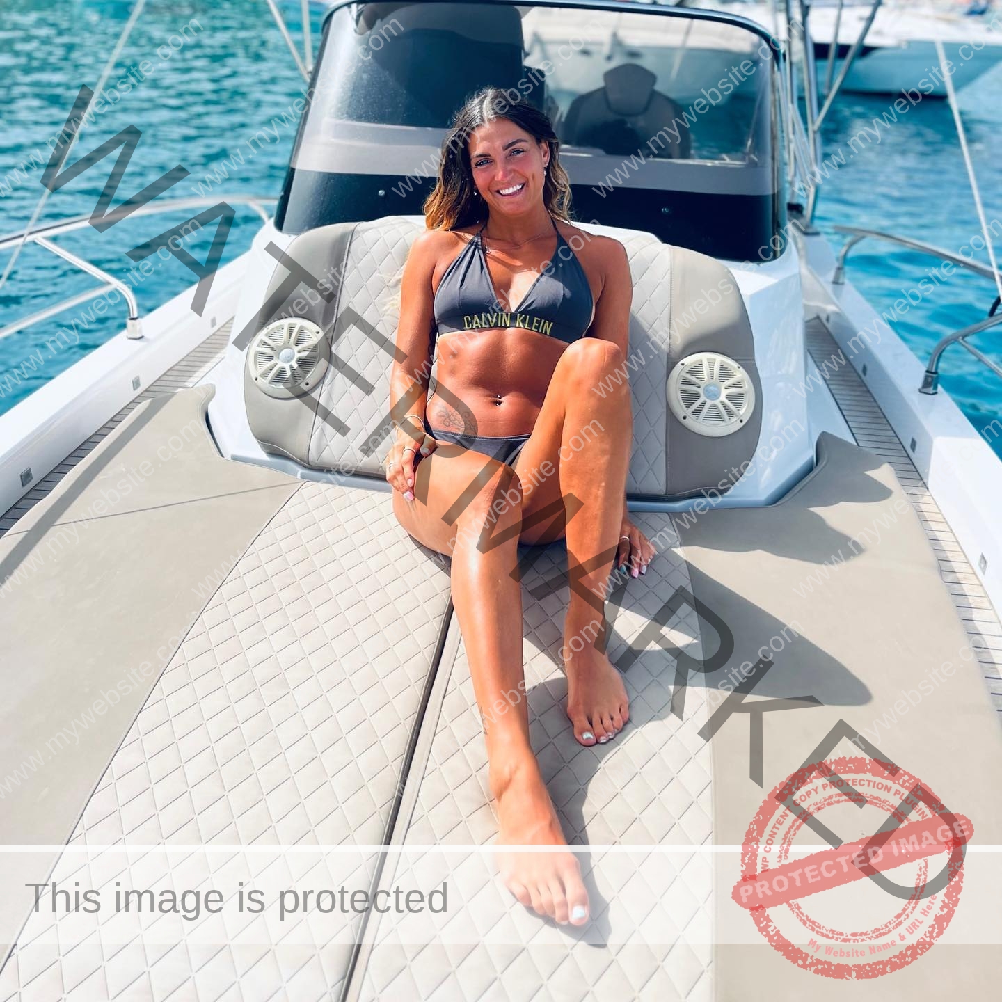 charlotte-wingfield-malta-charlottewingfield.oly-03889 Charlotte Wingfield, track athlete from Malta, is sitting and smiling on a boat deck in a gray bikini, blue water behind her.