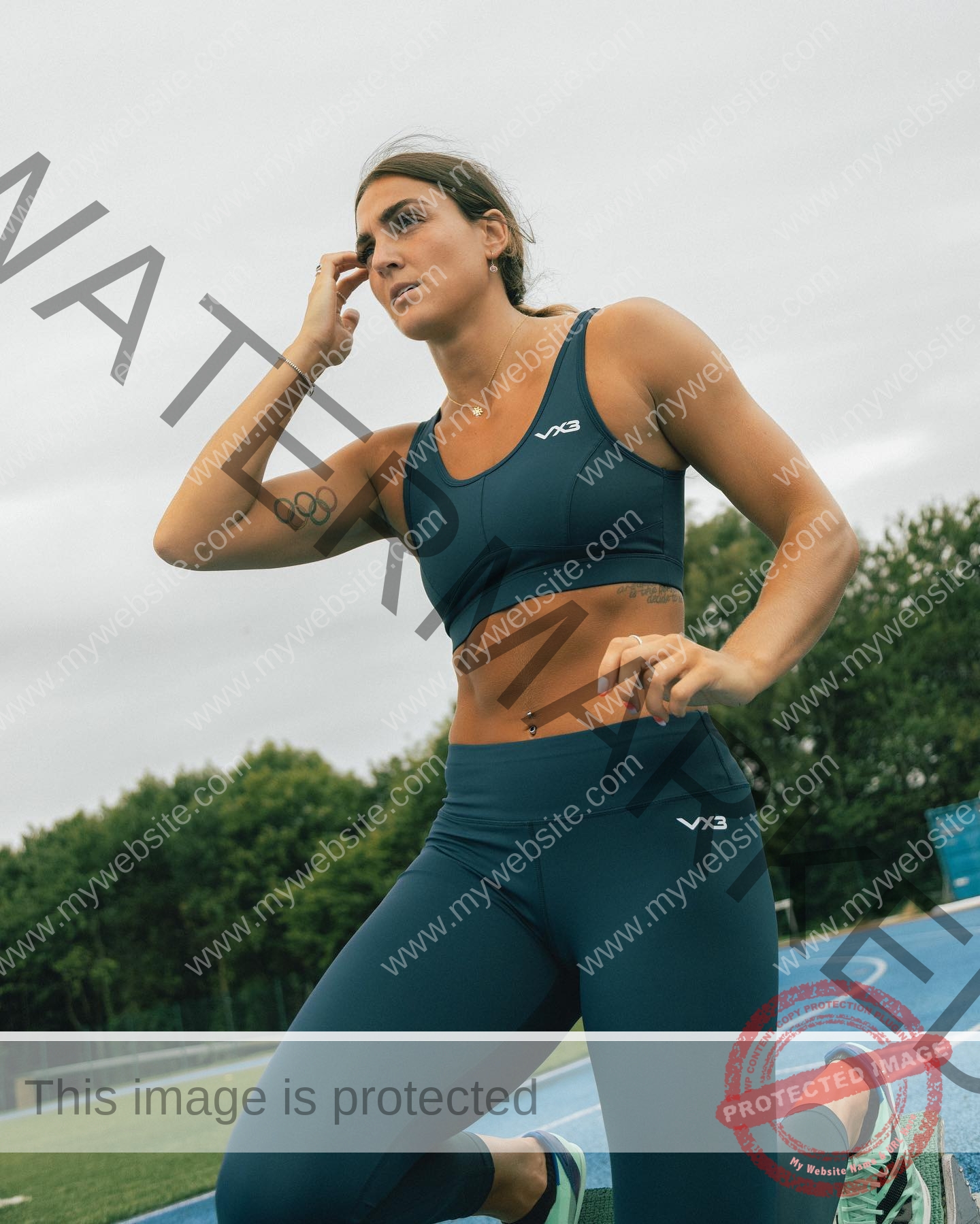 charlotte-wingfield-malta-charlottewingfield.oly-03913 Charlotte Wingfield, track athlete from Malta, in dark teal athletic wear kneels on a blue track, looking thoughtful under cloudy skies.