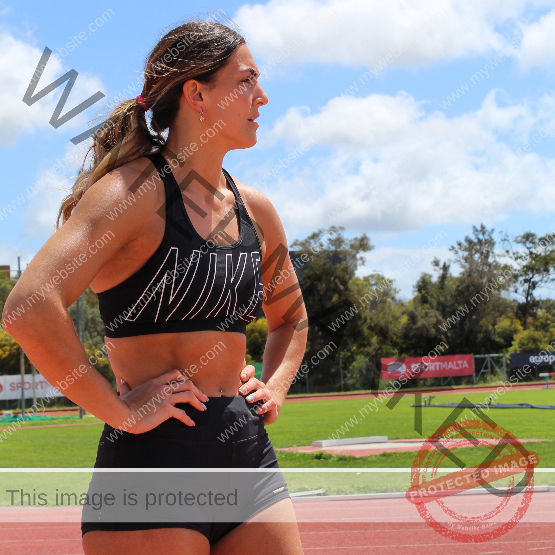charlotte-wingfield-malta-charlottewingfield.oly-03933 Charlotte Wingfield, track athlete from Malta, stands on a running track in black Nike gear, hands on hips, gazing into the distance.