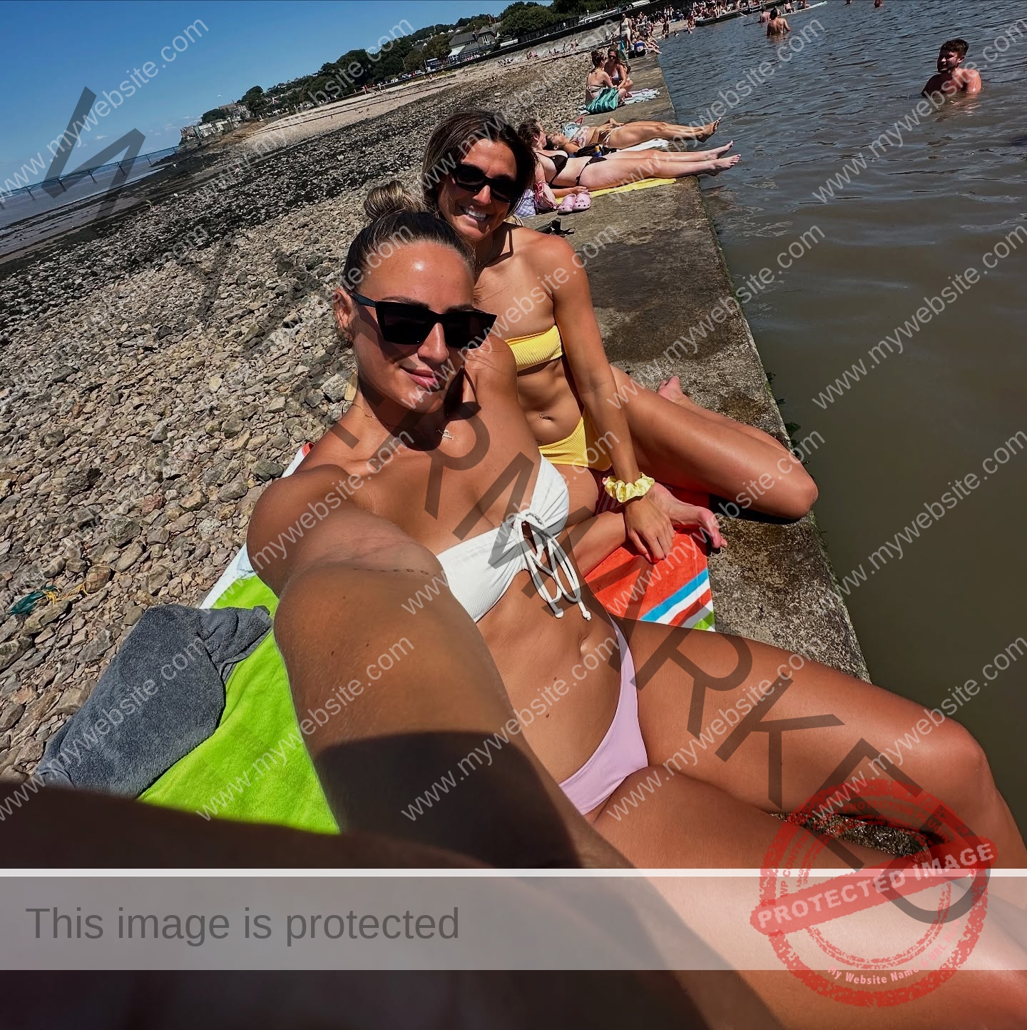 charlotte-wingfield-malta-charlottewingfield.oly-04080 Charlotte Wingfield, track athlete from Malta, two women in swimsuits and sunglasses take a selfie by a pebbled beach on a sunny day.