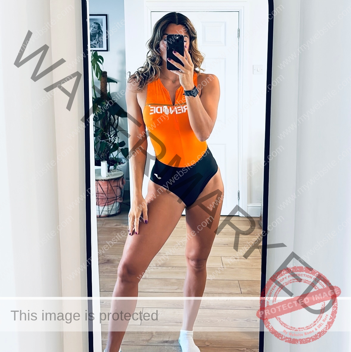 charlotte-wingfield-malta-charlottewingfield.oly-04085 Charlotte Wingfield, track athlete from Malta, stands in front of a mirror wearing an orange and black swimsuit and one white sock.