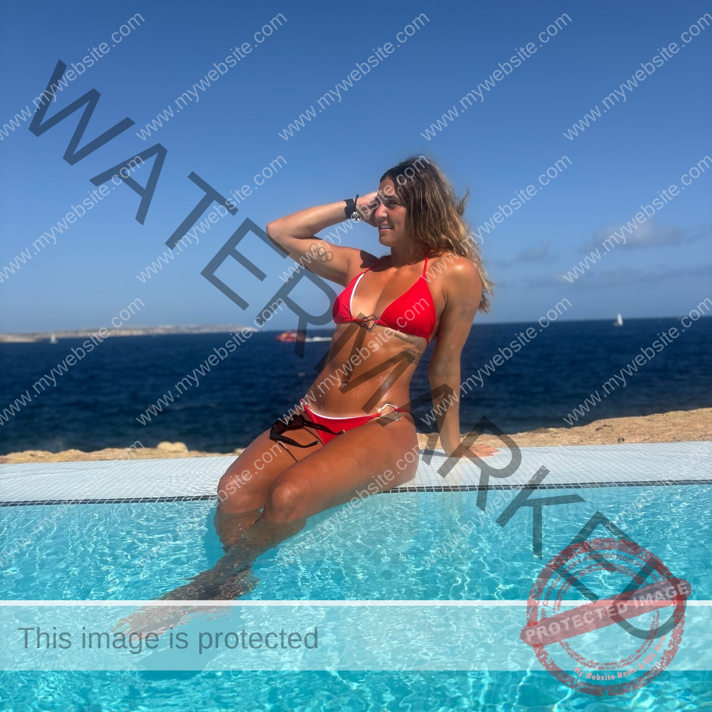 charlotte-wingfield-malta-charlottewingfield.oly-04118 Charlotte Wingfield, track athlete from Malta, sits in a red bikini by the pool, smiling with one hand in her hair, ocean behind.
